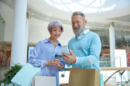 Happy elderly couple with phone comparing prices online during shoppingの写真素材