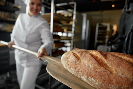 Closeup view on freshly baked artisan bread on shovel in female baker hands
