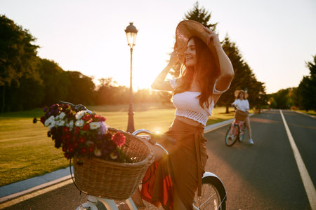 Female friends cycling together along local road at sunsetの写真素材