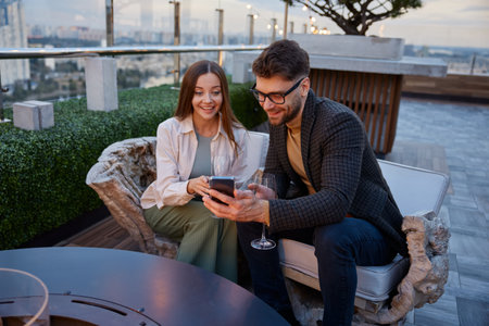 Couple engaged in friendly conversation using phone sitting on top of building