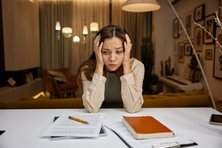 Worried stressed young woman freelancer looking on paper sitting at home table