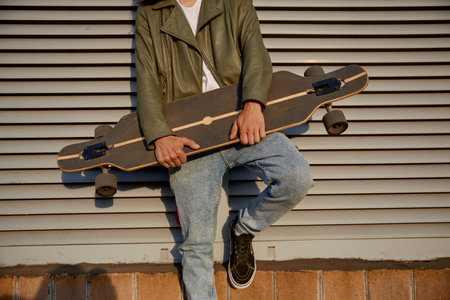 Crop of urban skater man posing for camera with longboard
