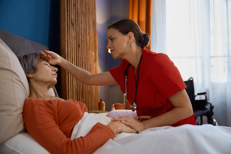 Female caregiver measuring temperature touching forehead of old womanの写真素材