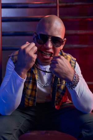 Portrait of young handsome hipster man with bald head biting beads