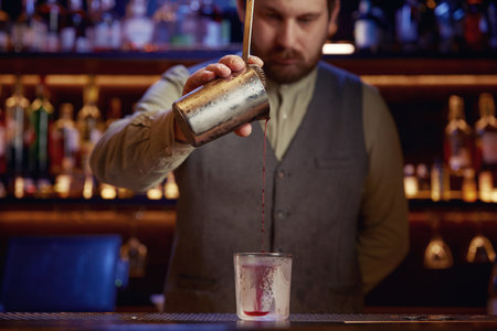 Elegant serious bartender pouring syrup from mix cup into glass