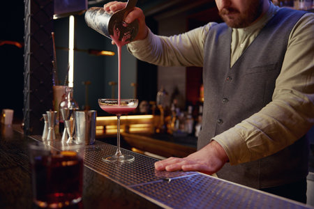Barman preparing fresh cocktail cosmopolitan into traditional glass