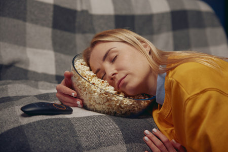 Sleepy woman is resting holding her head in plate with popcornの写真素材