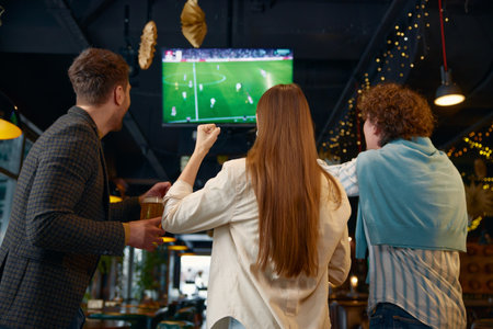 Happy excited group of friends watching football match on tv in pub