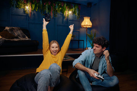 Young couple playing video game using joysticks together, woman proud because of victory against her...