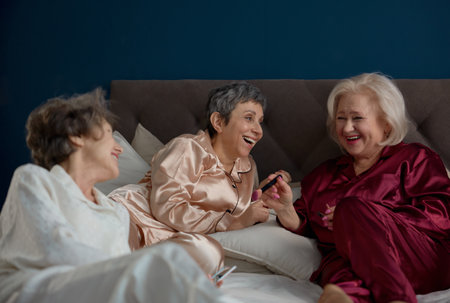 Retired female friends applying nail polish while having playful time at homeの写真素材