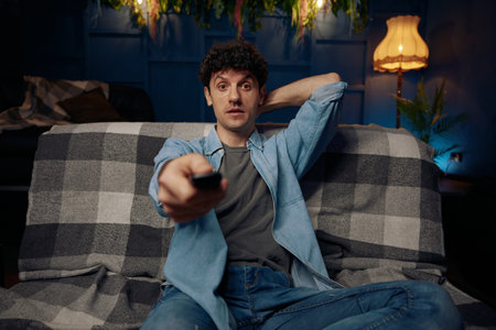 Man lounges on a comfortable couch, holding a remote controlの写真素材