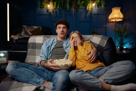 Scared couple watching TV in living roomの写真素材