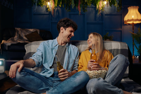 Man and woman couple sitting on a couch eating popcorn and drinking beerの写真素材