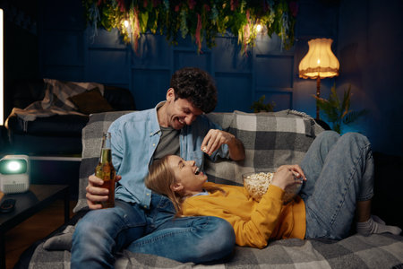 A couple sit on a comfortable couch enjoy popcorn and beerの写真素材