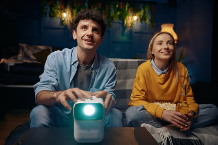 Man and a woman are sitting on a couch watching a movie on a projectorの写真素材