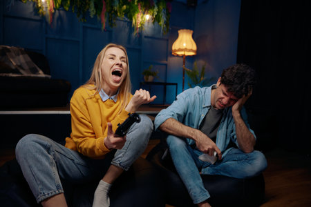 Young couple playing video game using joysticks together, woman proud because of victory against her boyfriendの写真素材