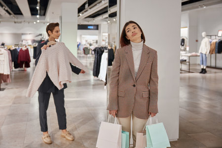 Young tired woman waiting for friend while shopping in clothes store