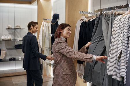 Enthusiastic young women friends choosing clothes during shopping at mall