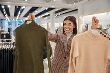 Portrait of glad satisfied woman holding new knitted sweaters on hangersの写真素材