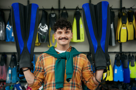 Portrait of hipster man holding flippers posing for camera over sportive shop