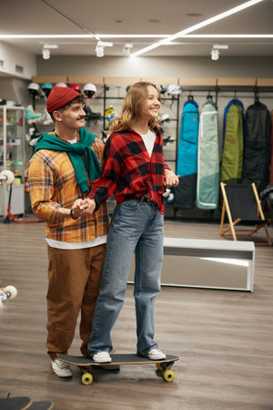 Young positive man and woman couple testing skate board in sport shop