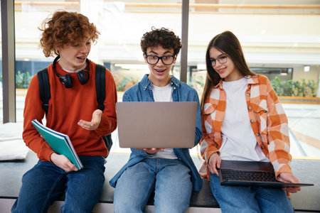 Three teenagers sitting in office looking at laptop discussing their work togetherの写真素材