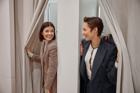 Happy young girlfriends in fitting room in clothing department store