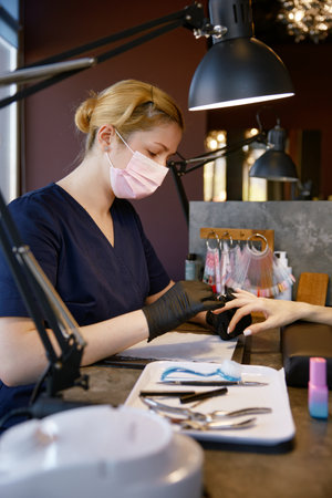 Manicurist in protective facial mask and gloves providing safety manicureの写真素材