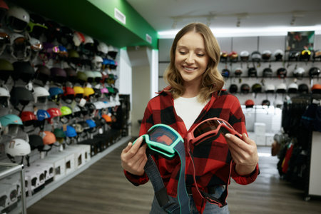 Young smiling woman choosing protective eye goggles mask at sports shop