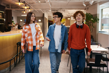 Three teenagers walking in modern office and discussing topical newsの写真素材