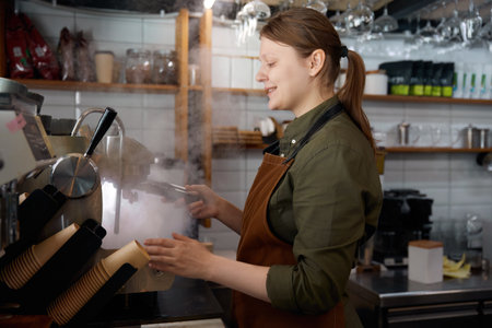 Young woman barista rinses tamper using hot water with steam from coffee machineの写真素材