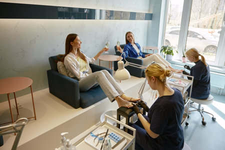 Two women clients deinking wine speaking at pedicure procedureの写真素材