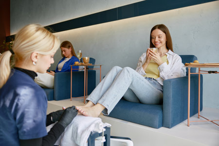 Two happy women clients deinking wine speaking at pedicure procedureの写真素材