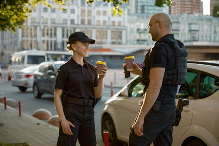Diverse young two patrol police officers drinking coffee enjoying break rest