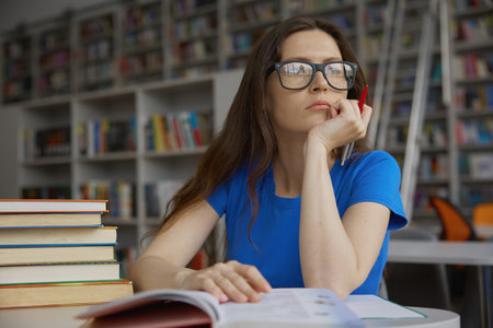 Smart woman in eyeglasses feeling dreamy while spending time in library