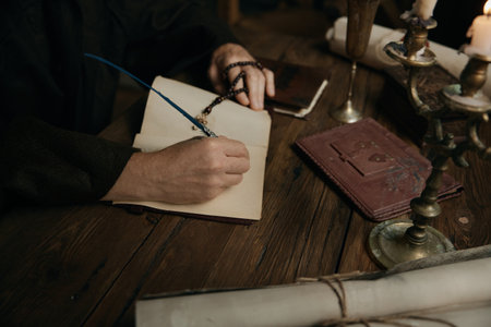 Crop shot of medieval monk chronicler writing ancient manuscript under candlelightの写真素材