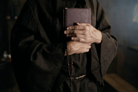 Priest holding closed bible book and rosary beads in hands closeupの写真素材