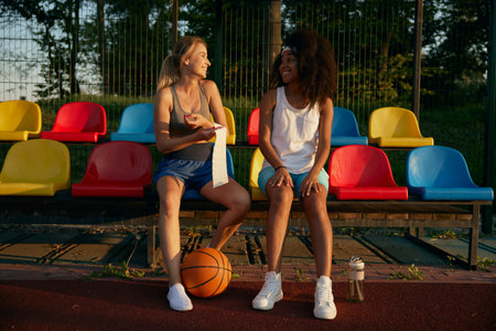 Female basketball players sitting at spectator seats having restの写真素材