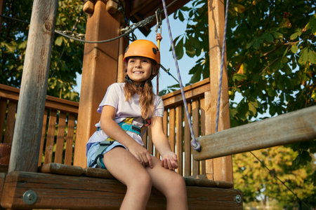 Relaxed girl child sitting on wooden rope playground taking breakの写真素材