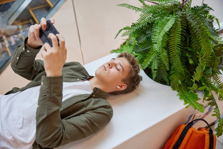 Teenage boy listening to music using smartphone resting in shopping mall