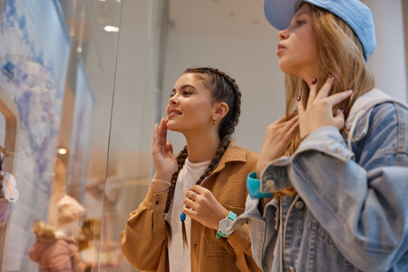 Happy teenage girls friends looking through showcase window in shopping mallの写真素材