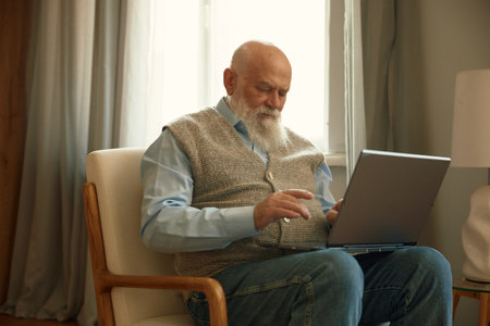 Retired senior man using laptop computer sitting on comfortable armchair at homeの写真素材