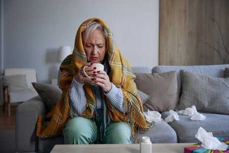 Sick elderly woman feeling weakness and fever symptoms drinking teaの写真素材