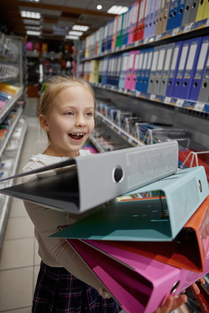Excited little girl child shopaholic carrying huge stack of foldersの写真素材