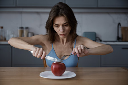 Young woman eating apple sitting at dining table in home kitchenの写真素材