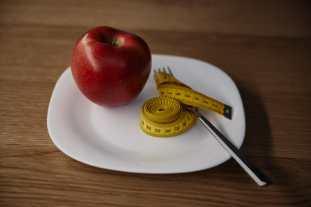 Apple and measuring tape on white plate served on wooden dining tableの写真素材