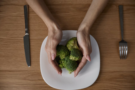 Female hands holding broccoli on the plate at home kitchenの写真素材