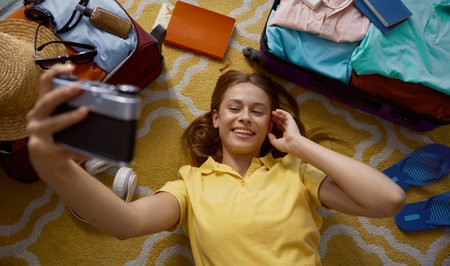 Young happy woman taking memory picture packing luggage for tripの写真素材