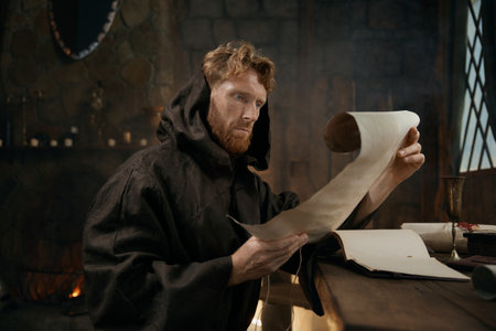 Medieval monk wearing robe with hood reading sacred manuscript on parchmentの写真素材