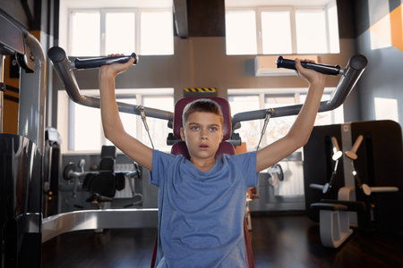 Teenager boy doing sports exercise at machine for chest muscles pumpingの写真素材